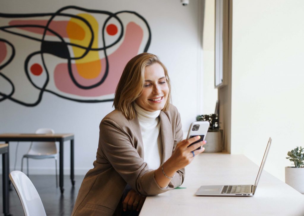 Mujeres sonriente en un café usa su celular para recibir el presupuesto de sus traducciones públicas portugués-español